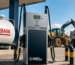 Fuel pump at a HomeBASE site, with a large white HomeBASE storage tank on the left and construction machinery in the background.