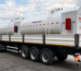 White tanker trailer attached to a multi-axle truck, used to haul liquids, with hazard placards on the rear.